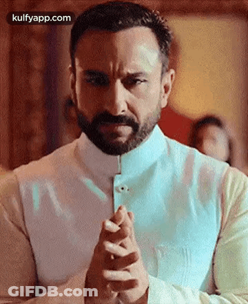 A Man With A Beard And Mustache Is Praying With His Hands Folded . GIF