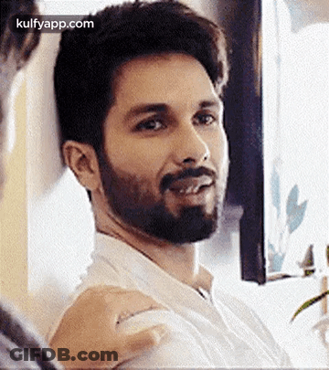 A Man With A Beard And Mustache Is Sitting In Front Of A Window And Smiling . GIF