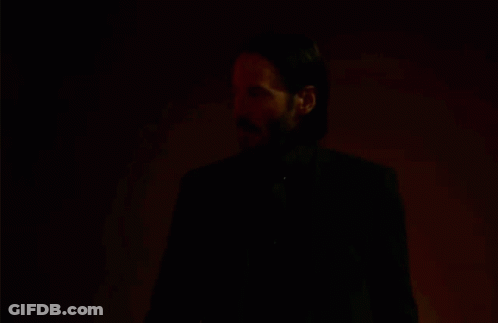 A Man With A Beard And Mustache Is Standing In A Dark Room . GIF