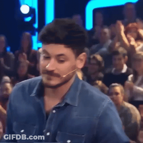 A Man With A Beard And Mustache Is Standing In Front Of A Crowd Of People GIF