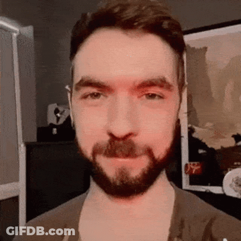 A Man With A Beard And Mustache Is Standing In Front Of A Framed Picture . GIF