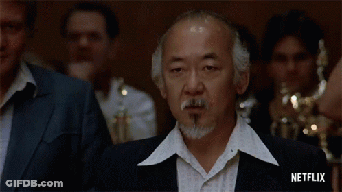 A Man With A Beard And Mustache Is Standing In Front Of A Group Of People . GIF
