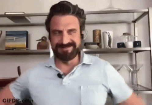 A Man With A Beard And Mustache Is Standing In Front Of A Shelf In A Room . GIF