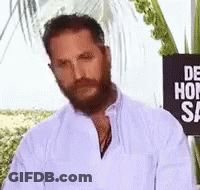 A Man With A Beard And Mustache Is Standing In Front Of A Sign That Says `` De Hon Sa '' . GIF