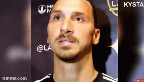 A Man With A Beard And Mustache Is Standing In Front Of A Sign That Says Kysta GIF