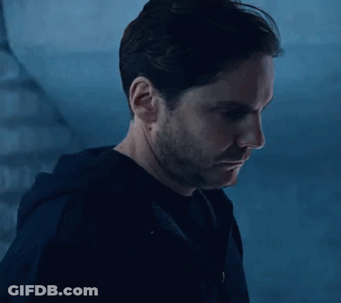 A Man With A Beard And Mustache Is Standing In Front Of A Staircase In A Dark Room . GIF