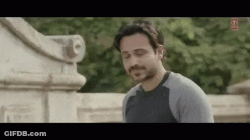 A Man With A Beard And Mustache Is Standing In Front Of A Stone Wall . GIF