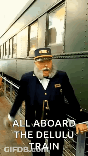 A Man With A Beard And Mustache Is Standing In Front Of A Train With The Words `` All Aboard The Delulu Train '' GIF