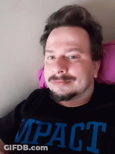 A Man With A Beard And Mustache Is Wearing A Black Impact Shirt GIF
