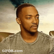 A Man With A Beard And Mustache Is Wearing A Grey Shirt And Looking At The Camera . GIF