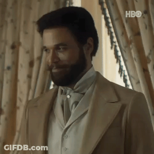 A Man With A Beard And Mustache Is Wearing A Suit And Tie . GIF