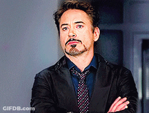 A Man With A Beard And Mustache Is Wearing A Suit And Tie With His Arms Crossed . GIF