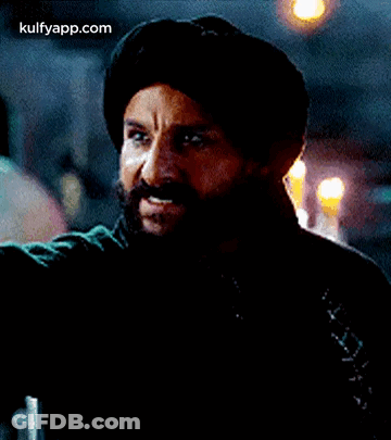A Man With A Beard And Mustache Is Wearing A Turban And A Black Jacket . GIF