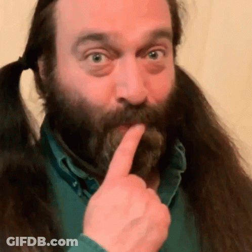 A Man With A Beard And Pigtails Is Holding His Finger To His Lips GIF
