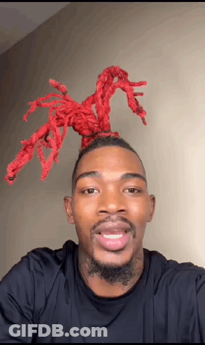 A Man With A Beard And Red Dreadlocks On His Head Is Smiling For The Camera . GIF