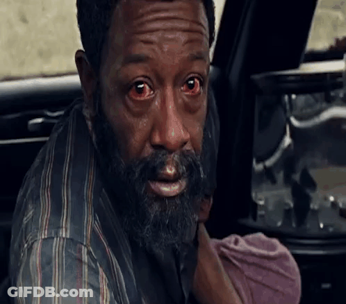A Man With A Beard And Red Eyes Is Holding A Baby In His Arms . GIF