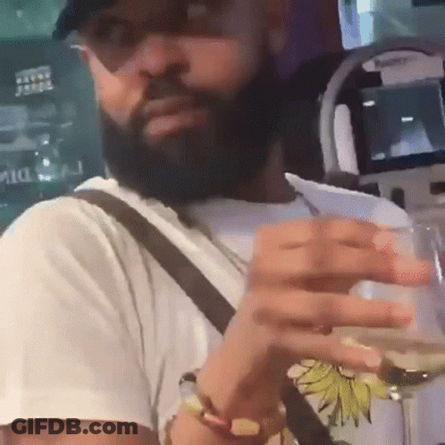 A Man With A Beard And Sunglasses Is Holding A Glass Of Wine GIF
