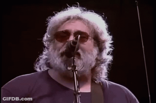 A Man With A Beard And Sunglasses Is Singing Into A Microphone On Stage . GIF