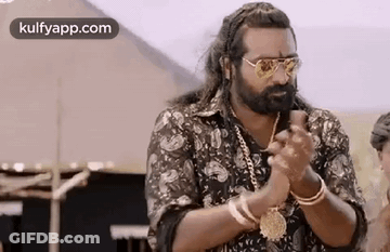 A Man With A Beard And Sunglasses Is Standing In Front Of A Tent And Clapping His Hands . GIF