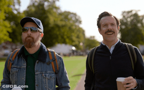 A Man With A Beard And Sunglasses Is Walking With Another Man GIF