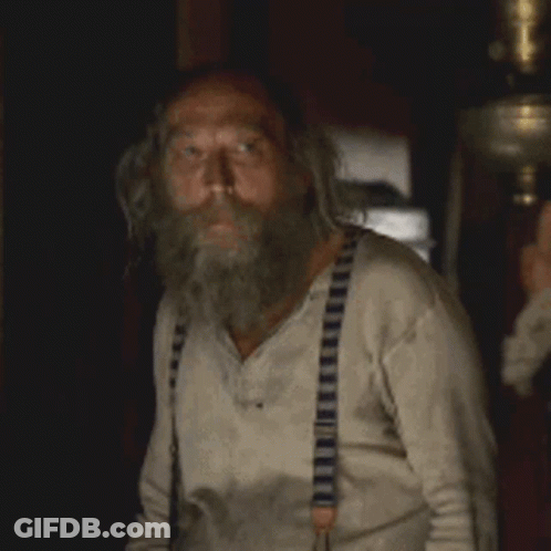 A Man With A Beard And Suspenders Is Looking At Something GIF