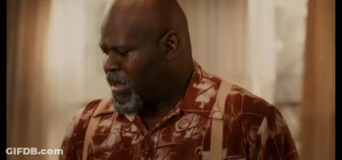 A Man With A Beard And Suspenders Is Standing In Front Of A Window In A Room . GIF