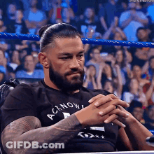 A Man With A Beard And Tattoos Is Sitting In A Chair In A Wrestling Ring . GIF