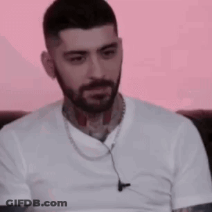 A Man With A Beard And Tattoos Is Wearing A White T-Shirt And Ear Buds . GIF
