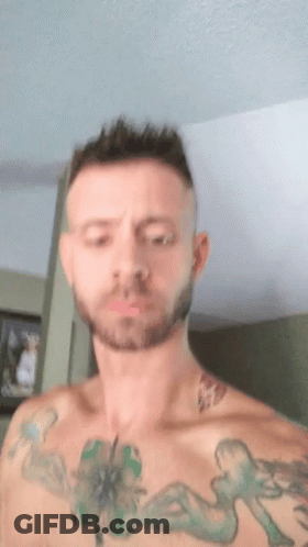 A Man With A Beard And Tattoos On His Chest Is Making A Funny Face . GIF