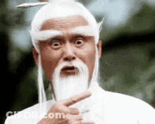 A Man With A Beard And White Hair Is Making A Funny Face And Pointing At Something . GIF