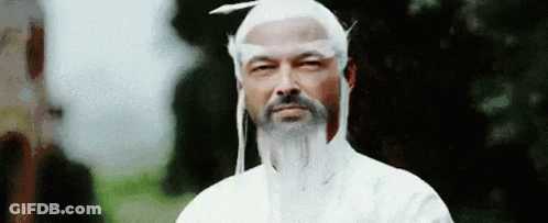 A Man With A Beard And White Hair Is Wearing A White Robe And A White Hat . GIF