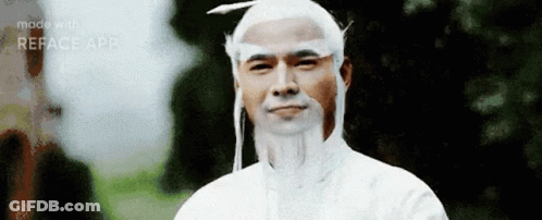 A Man With A Beard And White Hair Is Wearing A White Shirt And A White Hat . GIF