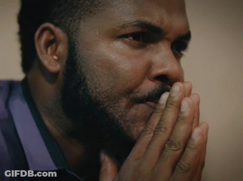 A Man With A Beard Has His Hands Folded In Front Of His Face GIF