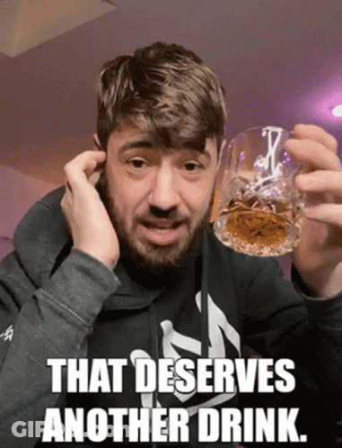 A Man With A Beard Holds A Glass Of Whiskey With The Caption That Deserves Another Drink GIF