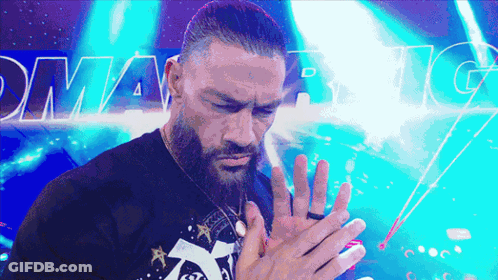 A Man With A Beard Holds His Hands Together In Front Of A Sign That Says Dynamite GIF