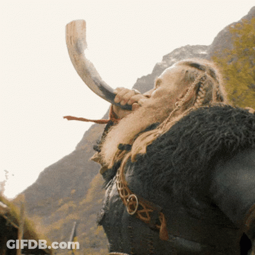 A Man With A Beard Is Blowing A Horn In Front Of Mountains GIF