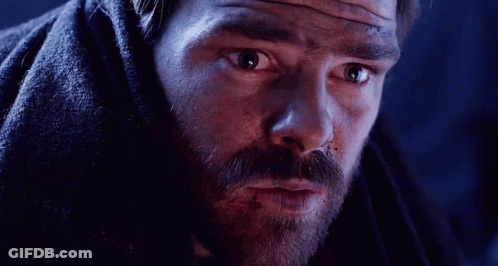 A Man With A Beard Is Covered In A Blanket And Looking At The Camera . GIF