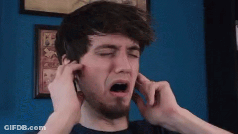 A Man With A Beard Is Covering His Ears With His Hands In Front Of A Blue Wall GIF