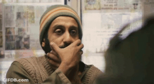 A Man With A Beard Is Covering His Mouth With His Hand While Looking At Another Man . GIF
