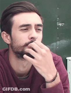A Man With A Beard Is Covering His Mouth With His Hand While Wearing A Maroon Shirt . GIF