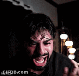 A Man With A Beard Is Crying In A Dark Room While Holding A Bottle . GIF