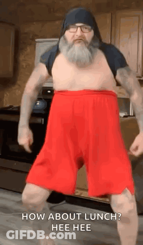 A Man With A Beard Is Dancing In A Kitchen Wearing Red Shorts . GIF