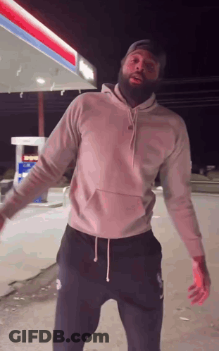 A Man With A Beard Is Dancing In Front Of A Gas Station . GIF