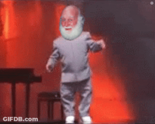 A Man With A Beard Is Dancing On A Stage With A Piano In The Background GIF