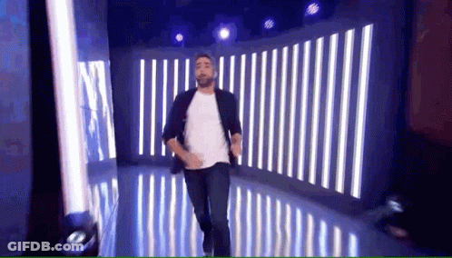 A Man With A Beard Is Dancing On A Stage With Striped Lights Behind Him . GIF