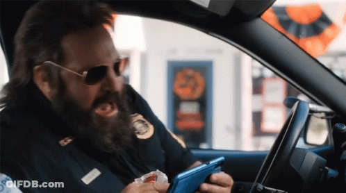 A Man With A Beard Is Driving A Car And Looking At His Cell Phone GIF