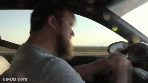A Man With A Beard Is Driving A Car And Looking Out The Window GIF
