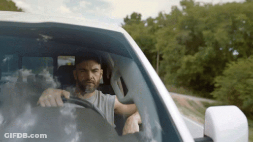 A Man With A Beard Is Driving A Car GIF