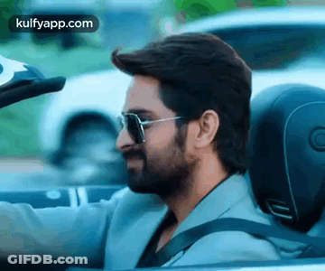 A Man With A Beard Is Driving A Convertible Car With Sunglasses On . GIF
