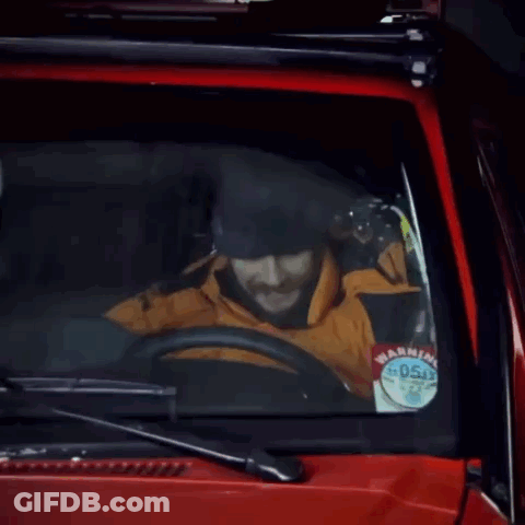 A Man With A Beard Is Driving A Red Car With The Words * Honk * Written On The Windshield GIF